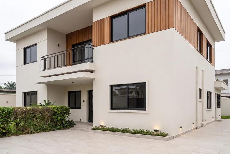 La même villa après travaux : enduit blanc lisse, bardage bois, menuiseries noires, dallage clair et éclairage encastré